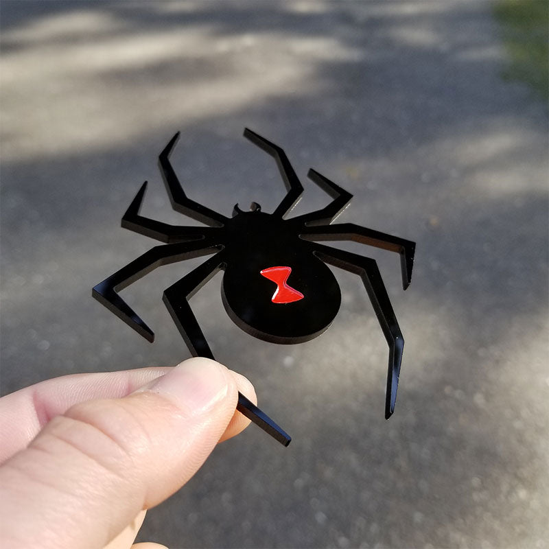 Hand holding a custom-made black spider emblem with a red hourglass from Yofab.