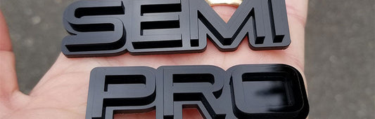 Gloss black Semi Pro automotive emblems in modern font style made from UV rated acrylic held outdoors.