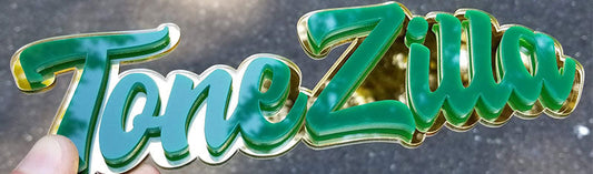 Tone-Zilla layered green script emblem with gold backing made from durable UV-rated acrylic held outdoors.