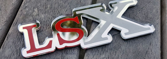Chrome LSX emblem inspired by classic GSX badge with color lettering and grille mounting standoffs displayed outdoors.