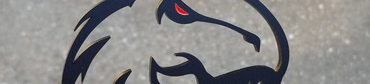 Matte black T-Rex head automotive emblem with red eye accent, precision-cut silhouette design held in hand outdoors.