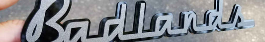 Gloss black and graphic acrylic 3D Badlands script emblem with layered dimensional design.
